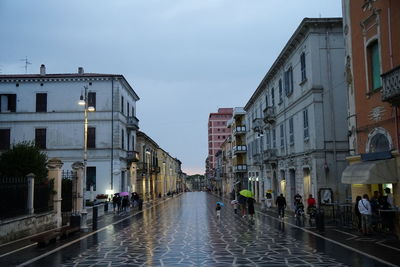 People walking on wet street amidst buildings during rainy season