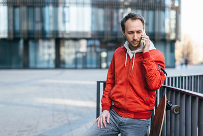 Stylish hipster in red jacket calling by the cell phone. urban and street photo. 