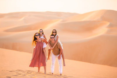 Rear view of women standing on sand at desert