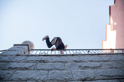 Full length of man climbing on wall against clear sky