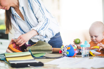 Midsection of busy mother holding fabric swatch while daughter playing at home office