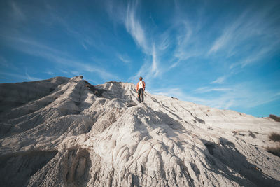 Man walking on rocks by mountains against sky