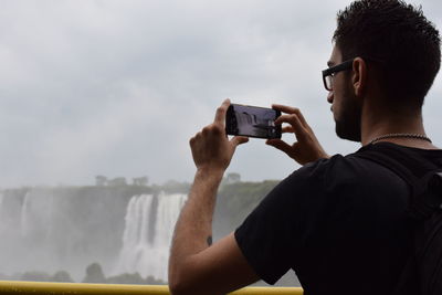 Midsection of man using mobile phone against a waterfall