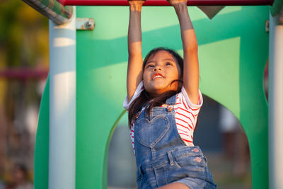 Cute girl hanging on monkey bars at playground