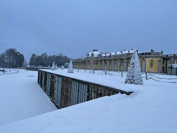 Snow covered field by building against sky