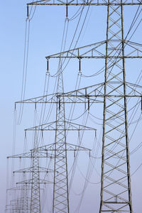 Low angle view of electricity pylon against clear blue sky