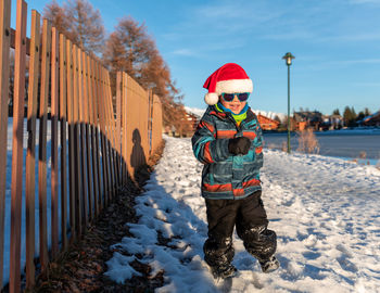 Cute boy wearing warm clothing standing on snow outdoors during winter