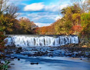 Scenic view of  beautiful waterfall, fall trees and clouds.