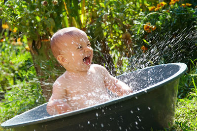 Cute baby boy splashing water while sitting in bucket