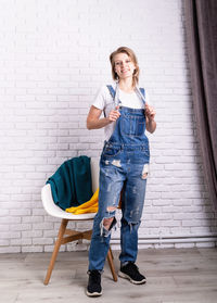 Full length portrait of a smiling young woman standing against wall