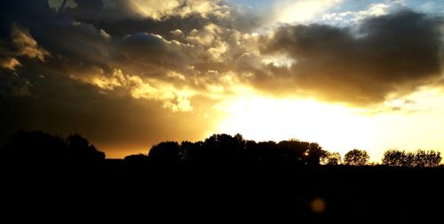 Silhouette trees against dramatic sky during sunset