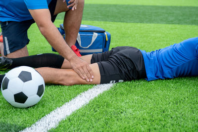 Low section of male physical therapist rubbing soccer player leg on field