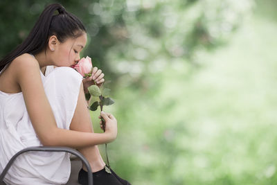 Side view of woman smelling rose at park