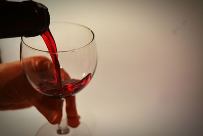 Cropped hand pouring red wine in glass against wall
