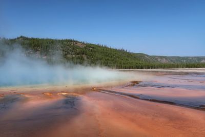 Landscape of orange sand and steam from a blue geyser pool in yellowstone national park