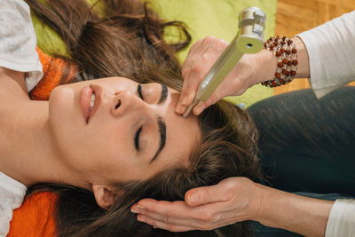 Midsection of therapist holding equipment on head of young woman at spa