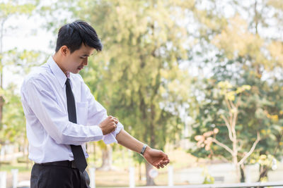 Side view of young businessman rolling up sleeve