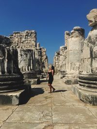 Woman walking amidst old ruin against clear blue sky