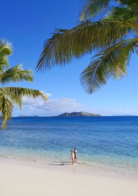 Girl and boy walking on beach against sky