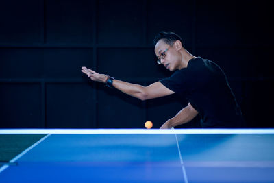 Young man playing table tennis in dark