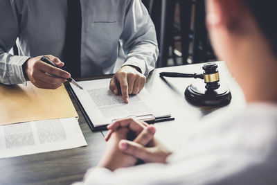 Midsection of judge pointing at document while worried client sitting on table