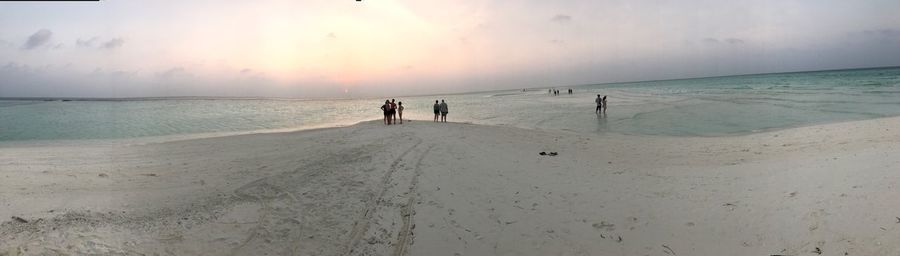 People at beach against sky during sunset