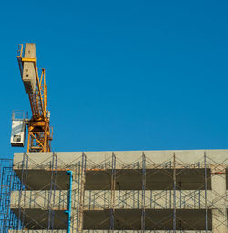 Low angle view of crane against building against clear blue sky