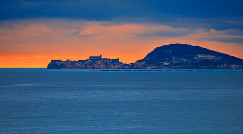 Scenic view of sea by buildings against sky during sunset