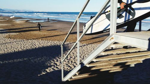 Low section of man climbing staircase of lifeguard hut with surfboard at beach