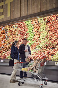 Man looking at woman talking on mobile phone while buying apples at supermarket