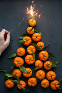 Christmas tree made from tangerines and sparkler, kept by female hand. flat lay on dark background. 