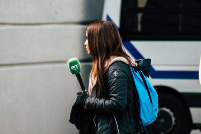 Rear view of woman with umbrella standing against wall