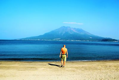 Rear view full length of man walking at beach on sunny day