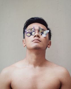 Shirtless man with artificial butterflies against gray wall