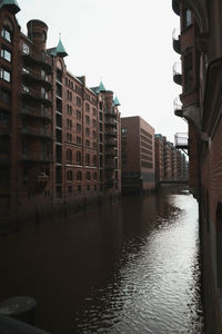 Canal by buildings against sky in city