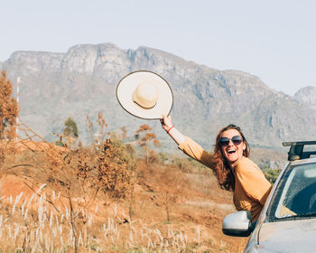 Woman with hat in hand with body getting out of the car with serra do caraça in the background
