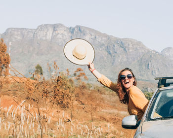 Portrait of smiling young woman using mobile phone while standing against sky