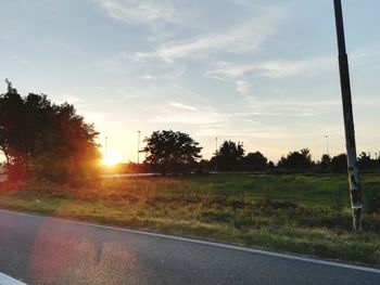 Road by trees on field against sky during sunset