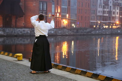 Rear view of man practicing martial arts while standing on bridge in city during sunset