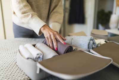 Hand of woman arranging rolled up cloths in bag on bed