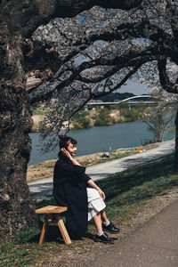 Woman sitting on bench against trees