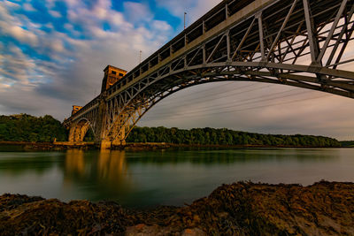 Low angle view of bridge over river against cloudy sky