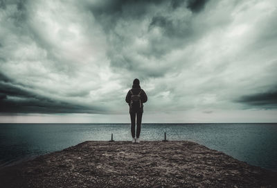 Rear view of woman standing at beach against cloudy sky