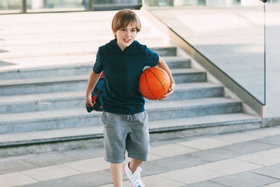 Boy holding basketball ball while walking on road