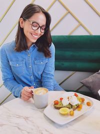 Smiling young woman with breakfast sitting at table