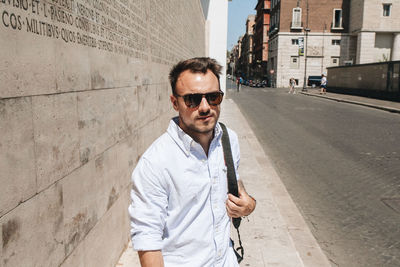 Portrait of young man wearing sunglasses standing against wall