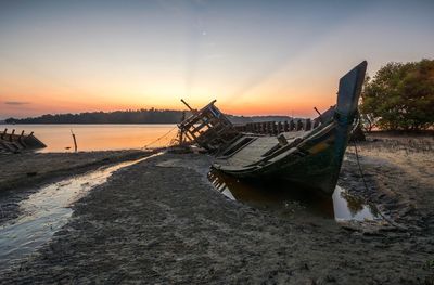 Boat moored on beach against sky during sunset