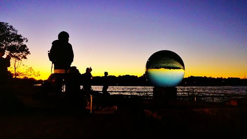 Silhouette people standing by sea against clear sky during sunset