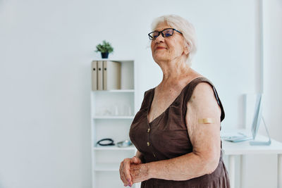 Mid adult woman looking away while standing against wall at home