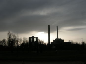 Silhouette industrial buildings against cloudy sky at dusk